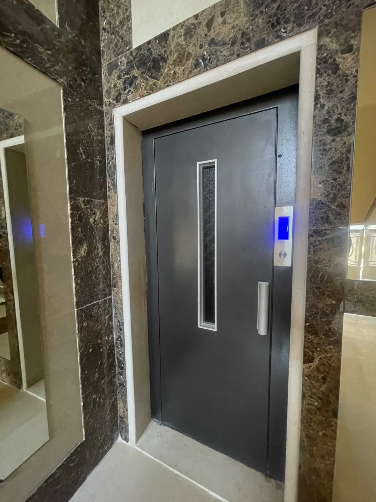 Dark elevator landing door with a slim vision panel and blue floor indicator